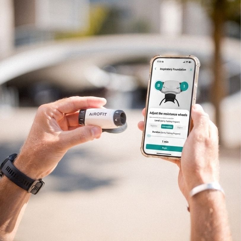 Airofit Atemtrainer in weiß und schwarz, gehalten in einer Hand, daneben ein Smartphone mit der Airofit App.