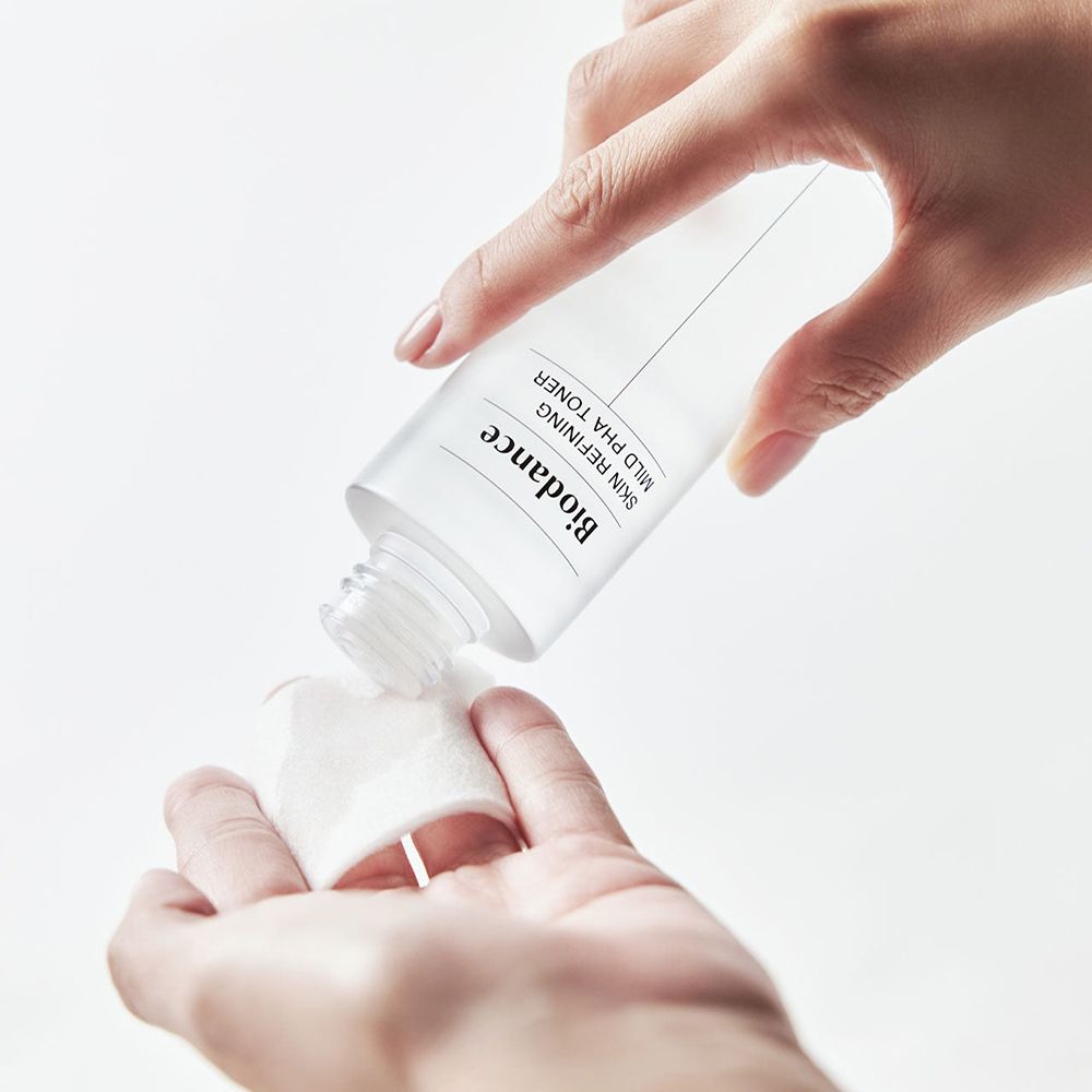 Hände halten eine Flasche Biodance Toner und ein Wattepad. Toner wird auf das Pad gegossen.