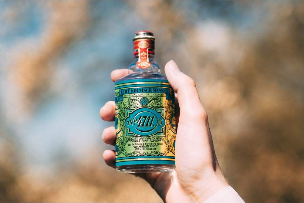 Eine Hand hält eine kleine Flasche Echt Kölnisch Wasser. Aufschrift: No. 4711, Echt Kölnisch Wasser. Flasche mit roter und goldener Verzierung.