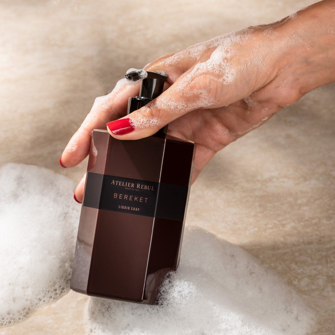 Bordeauxfarbene Flüssigseife mit schwarzem Pumpkopf. Hand mit Seifenschaum. Aufschrift: Atelier Rebul Bereket.