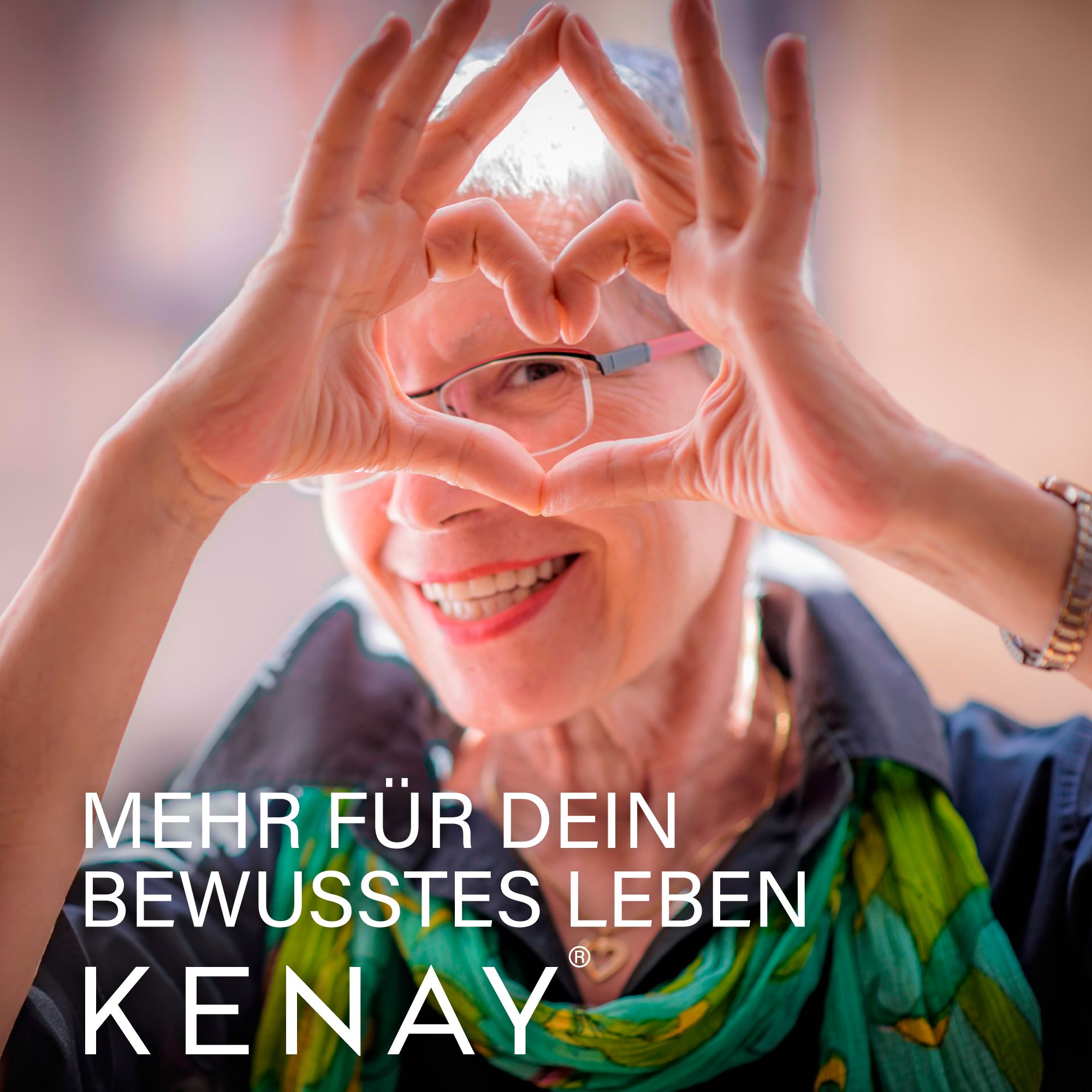 Ältere Frau formt Herz mit Händen. Schriftzug MEHR FÜR DEIN BEWUSSTES LEBEN, KENAY-Logo.