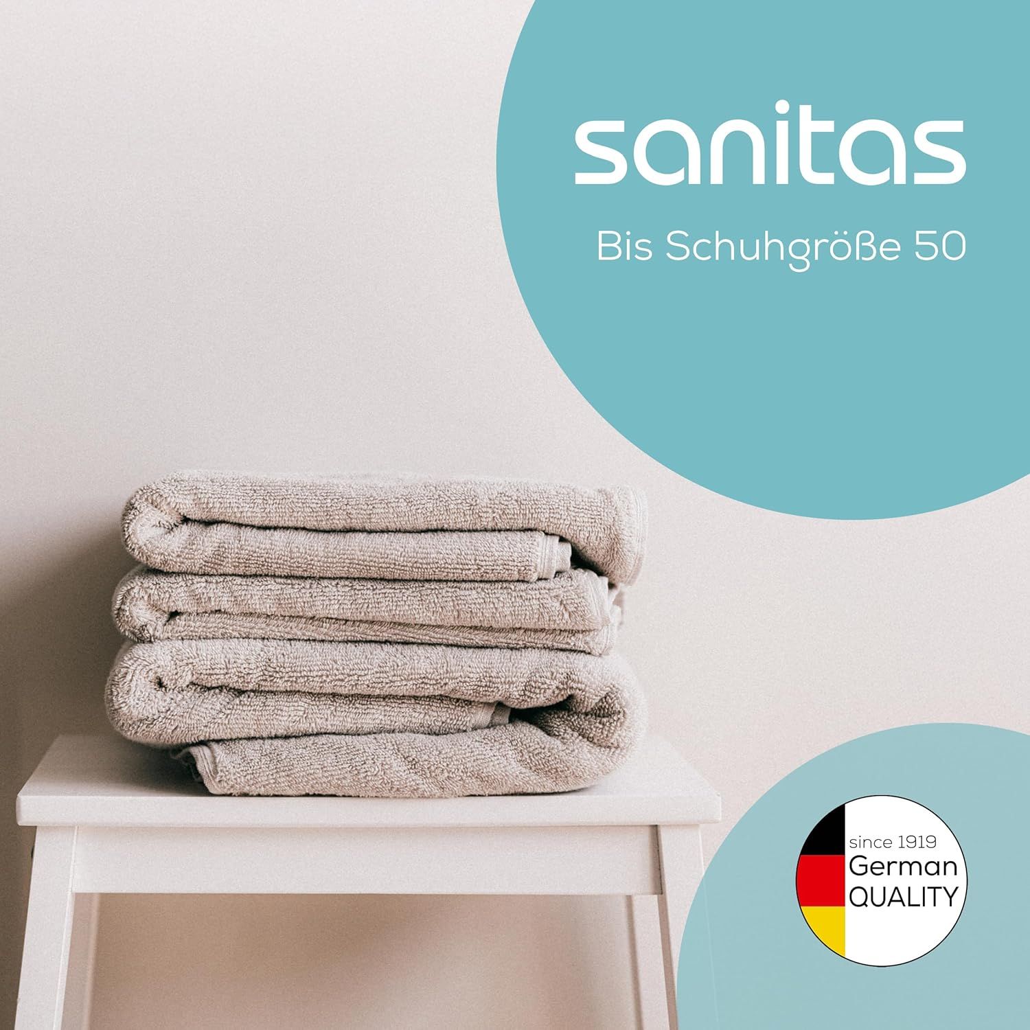 Stapel Handtücher auf Hocker. Sanitas-Logo. Text: Bis Schuhgröße 50. Qualitätszeichen.