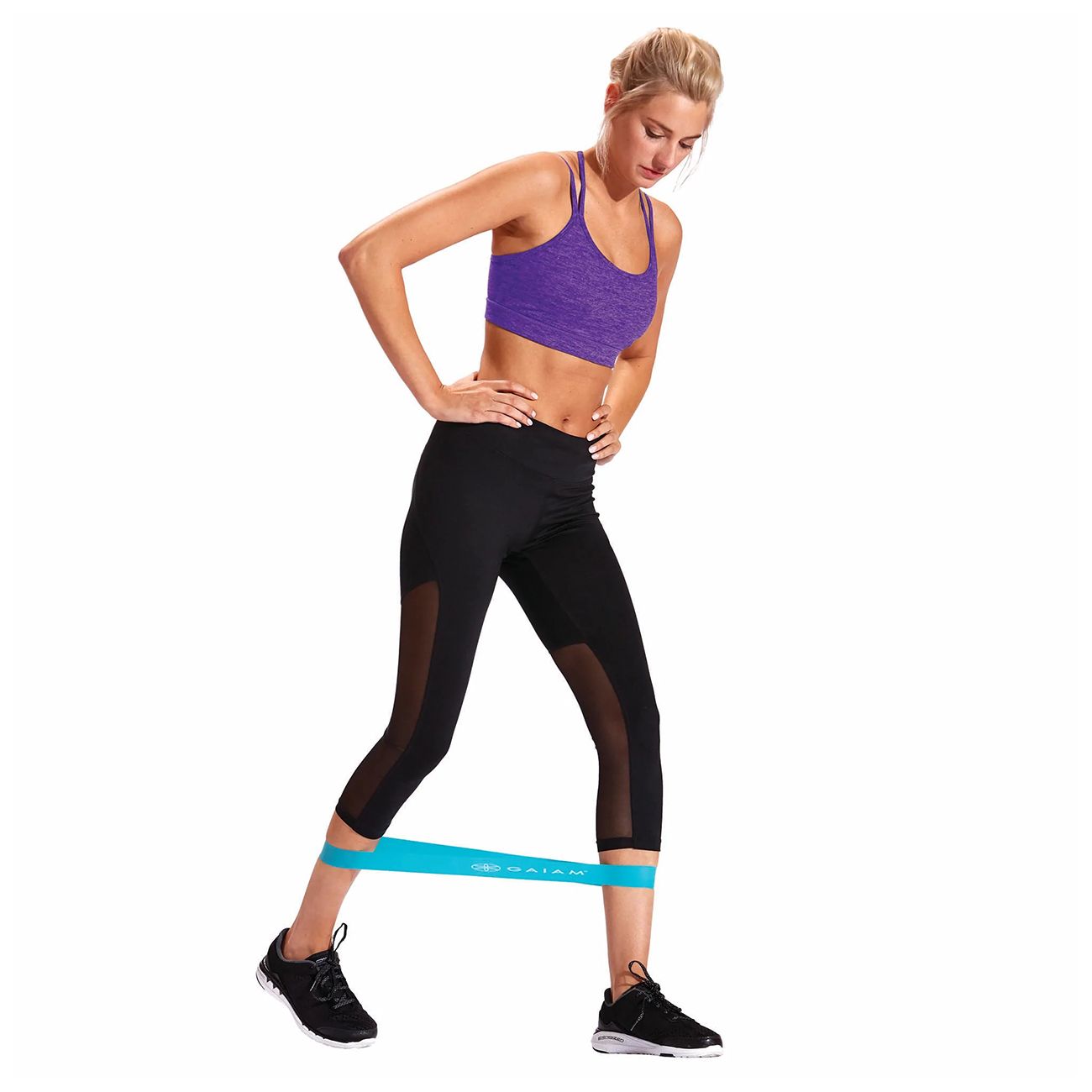 Frau trainiert mit blauem Fitnessband um die Knöchel. Schwarze Sportkleidung, violettes Top. Band mit Aufschrift.