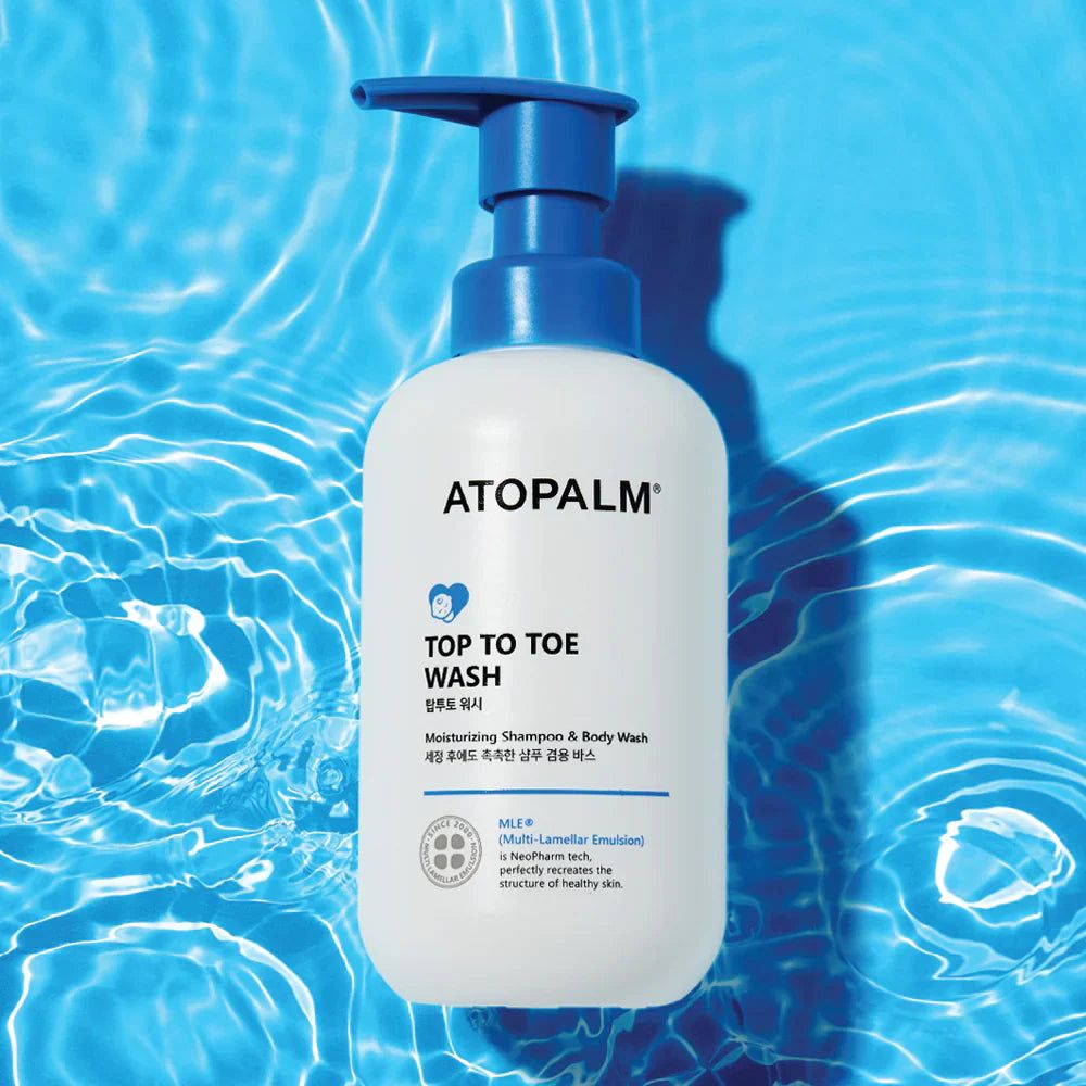 Weiße Flasche mit blauem Pumpkopf. Aufschrift: ATOPALM TOP TO TOE WASH. Hintergrund: Wassertextur.