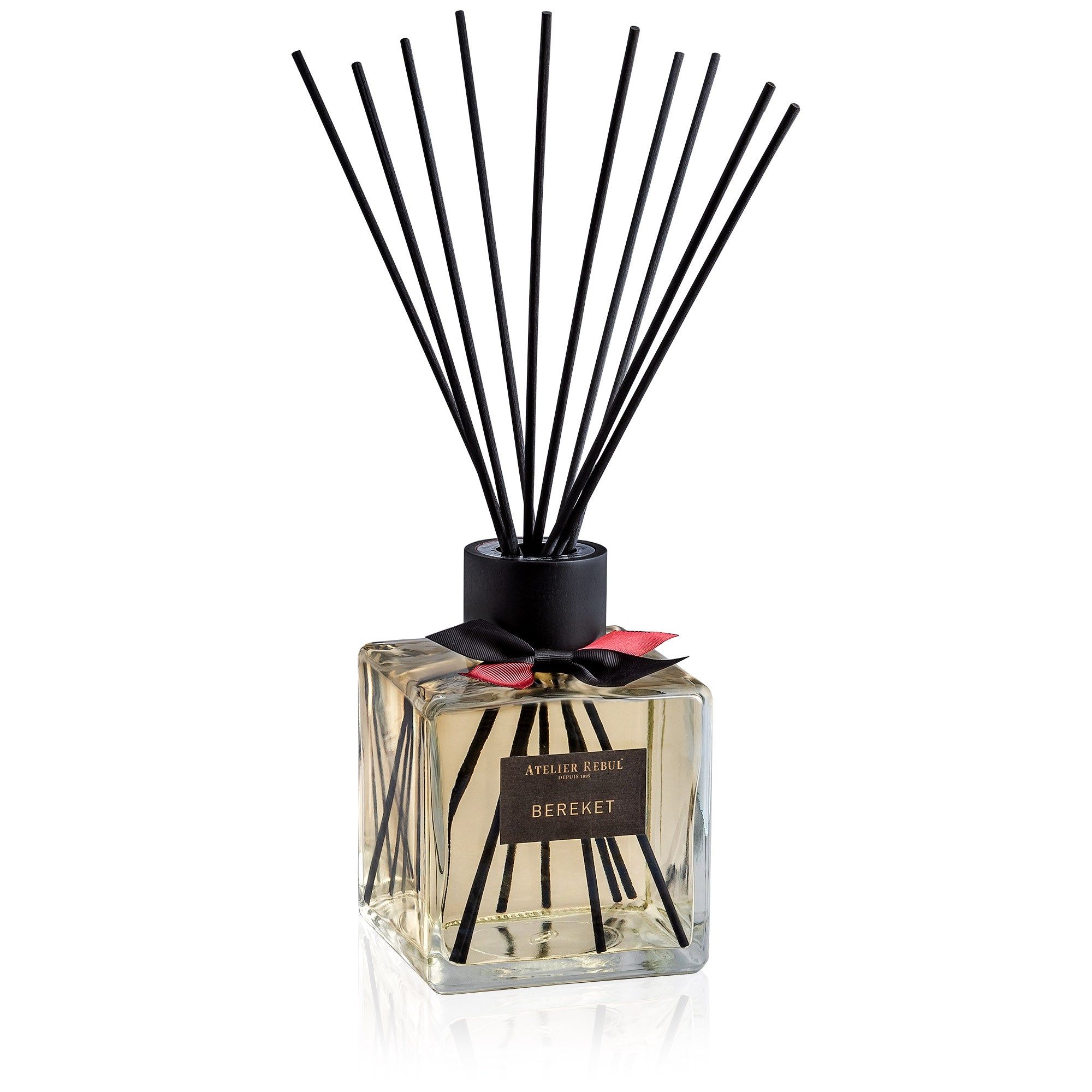 Quadratischer Glasbehälter mit schwarzen Stäbchen. Schwarze Schleife und Etikett mit Schriftzug. Produktname: Bereket.