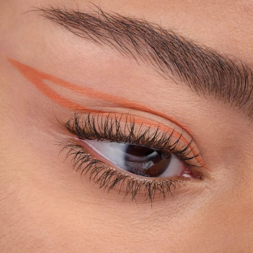 Auge mit orangefarbenem Eyeliner-Strich. Wimpern und Augenbraue sichtbar.