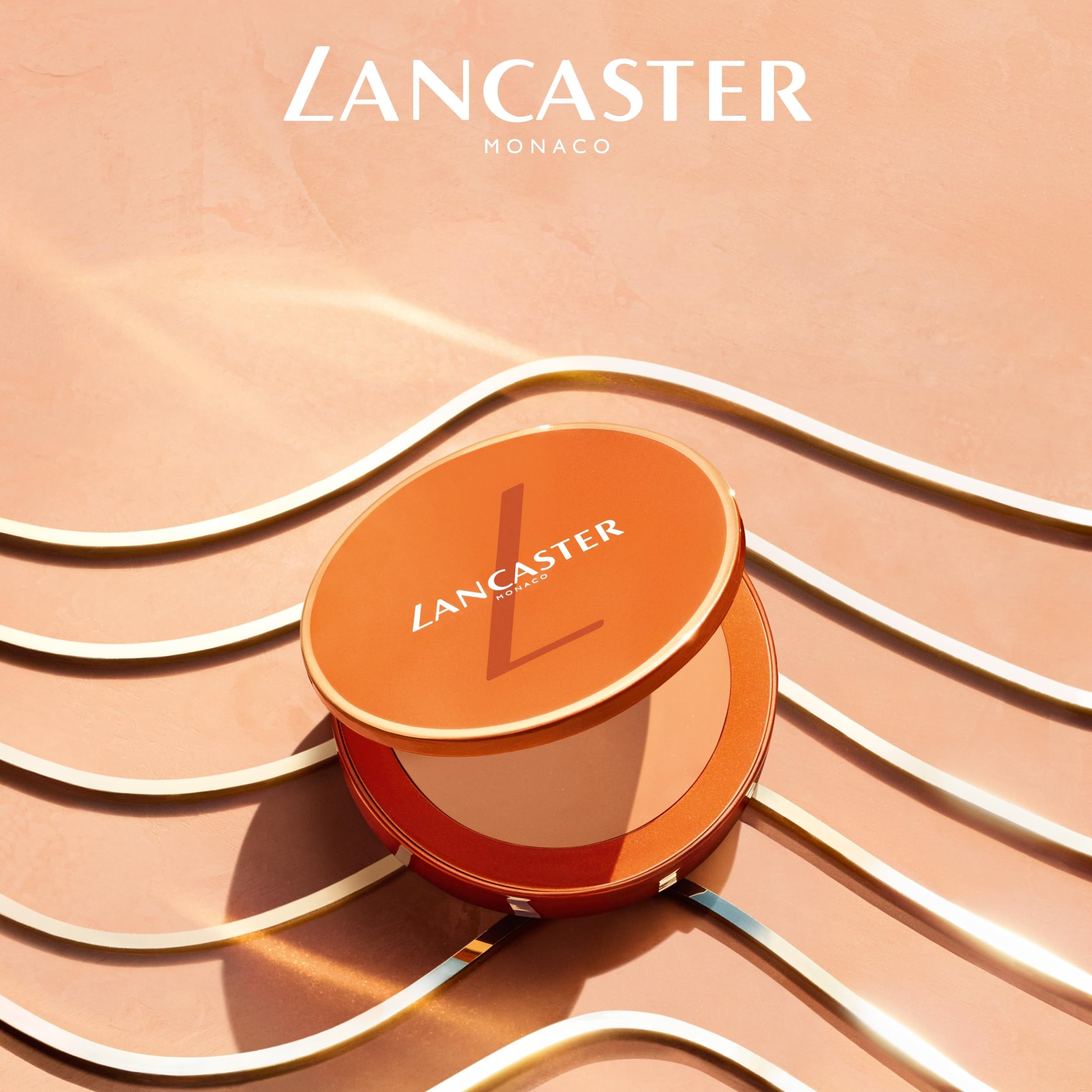 Geöffnete, orangefarbene Kompakt-Sonnencreme. Deckel mit LANCASTER-Logo. Innen: getönte Creme. Hintergrund: goldene Linien.