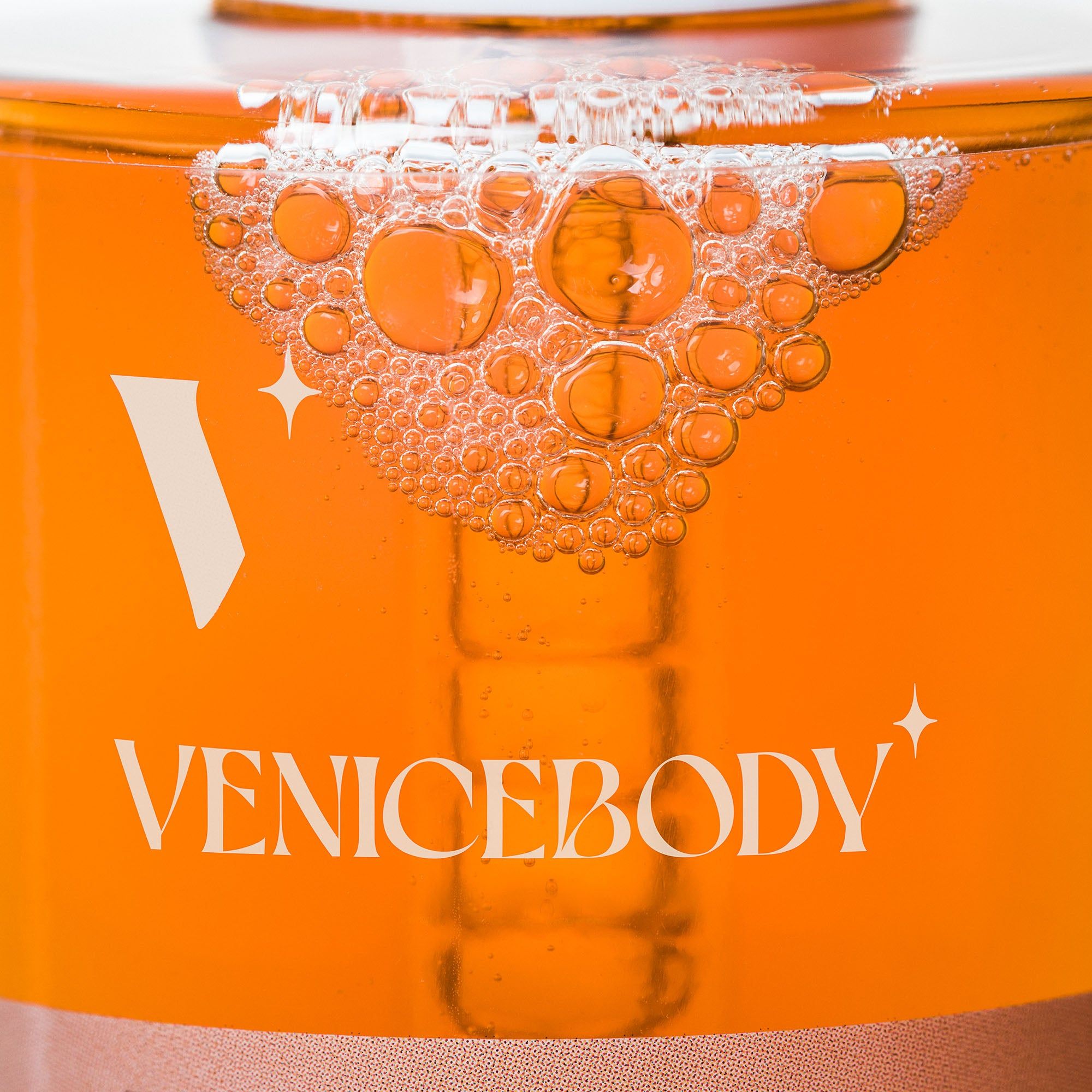 Nahaufnahme einer Glasflasche mit brauner Flüssigkeit. Aufschrift: VENICEBODY. Blasen auf der Flüssigkeit.