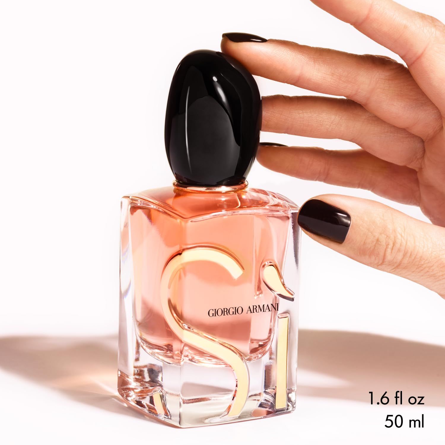 Giorgio Armani Si Eau de Parfum Intense. Flakon mit schwarzem Deckel und goldfarbenem Logo. 50 ml. Hand mit lackierten Nägeln.