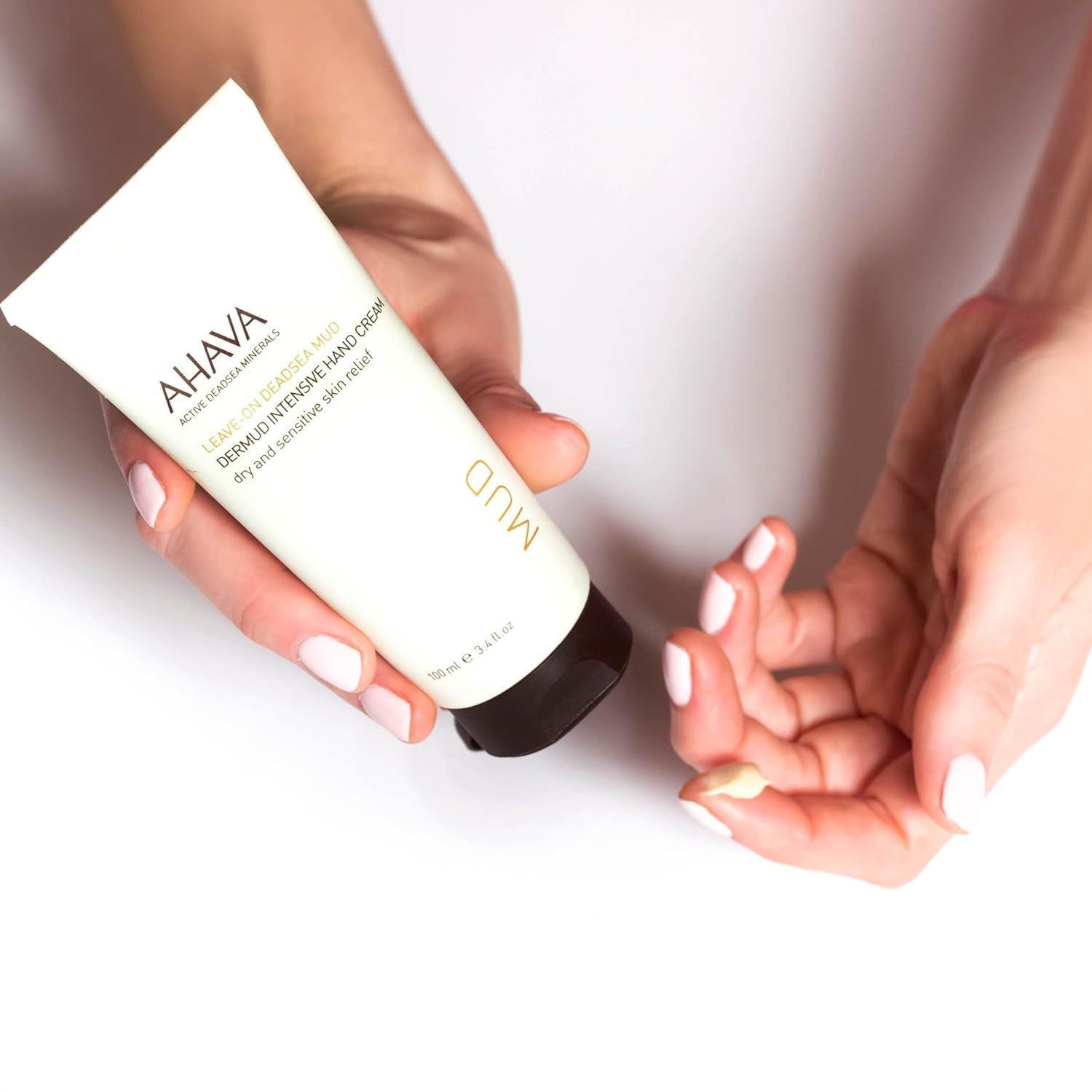 Hände halten AHAVA Dermud Intensive Hand Cream Tube. Creme auf Finger aufgetragen. Weißer Hintergrund.