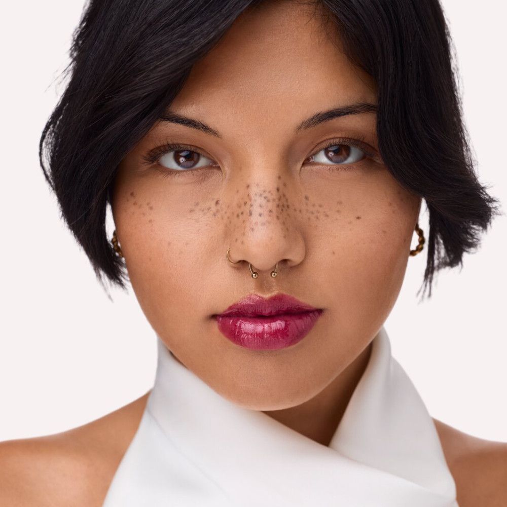 Porträt einer Frau mit rotem Lipgloss. Sie trägt einen weißen Schal und hat Sommersprossen im Gesicht.