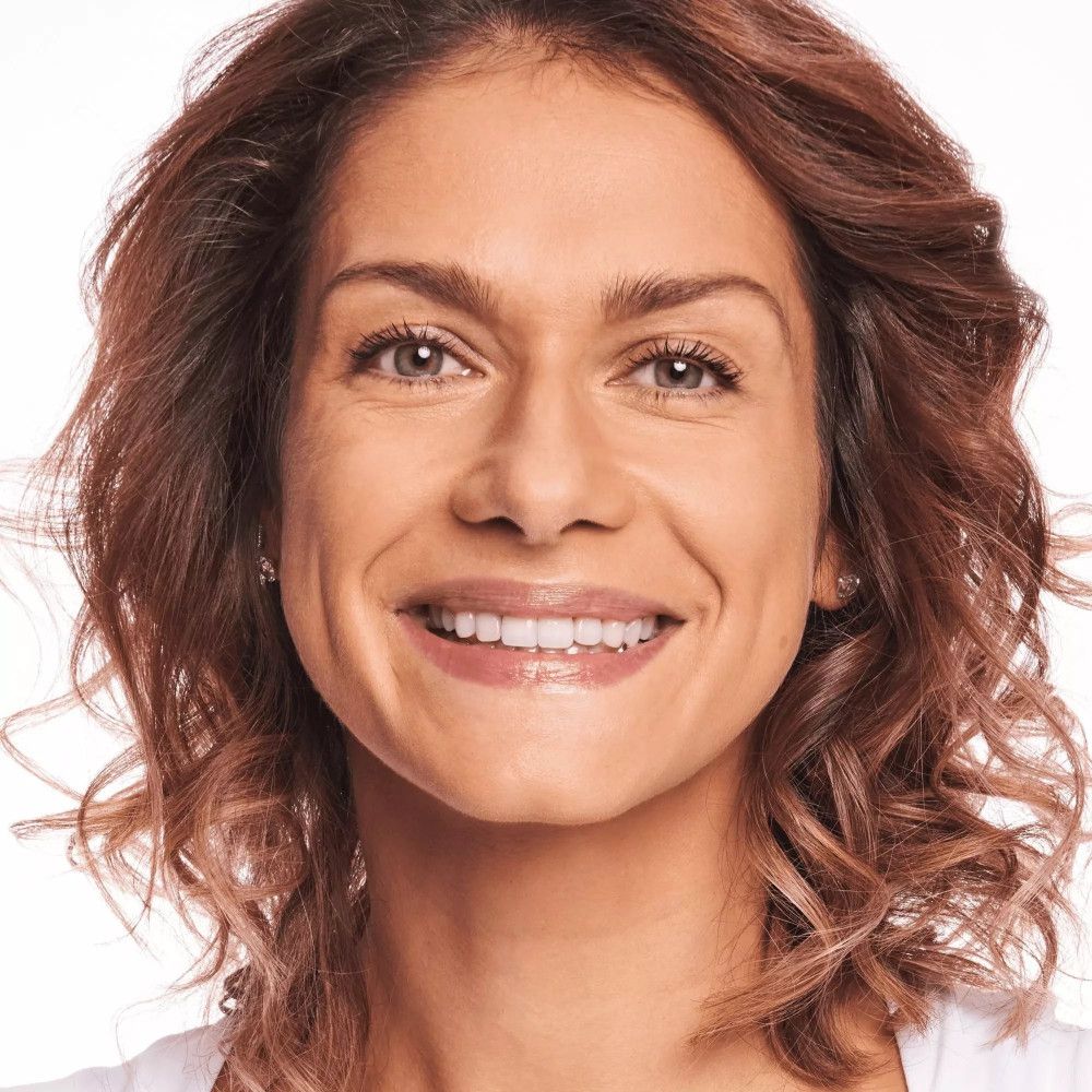 Porträt einer lächelnden Frau. Sie trägt Make-up. Helle Haut, braune Haare.