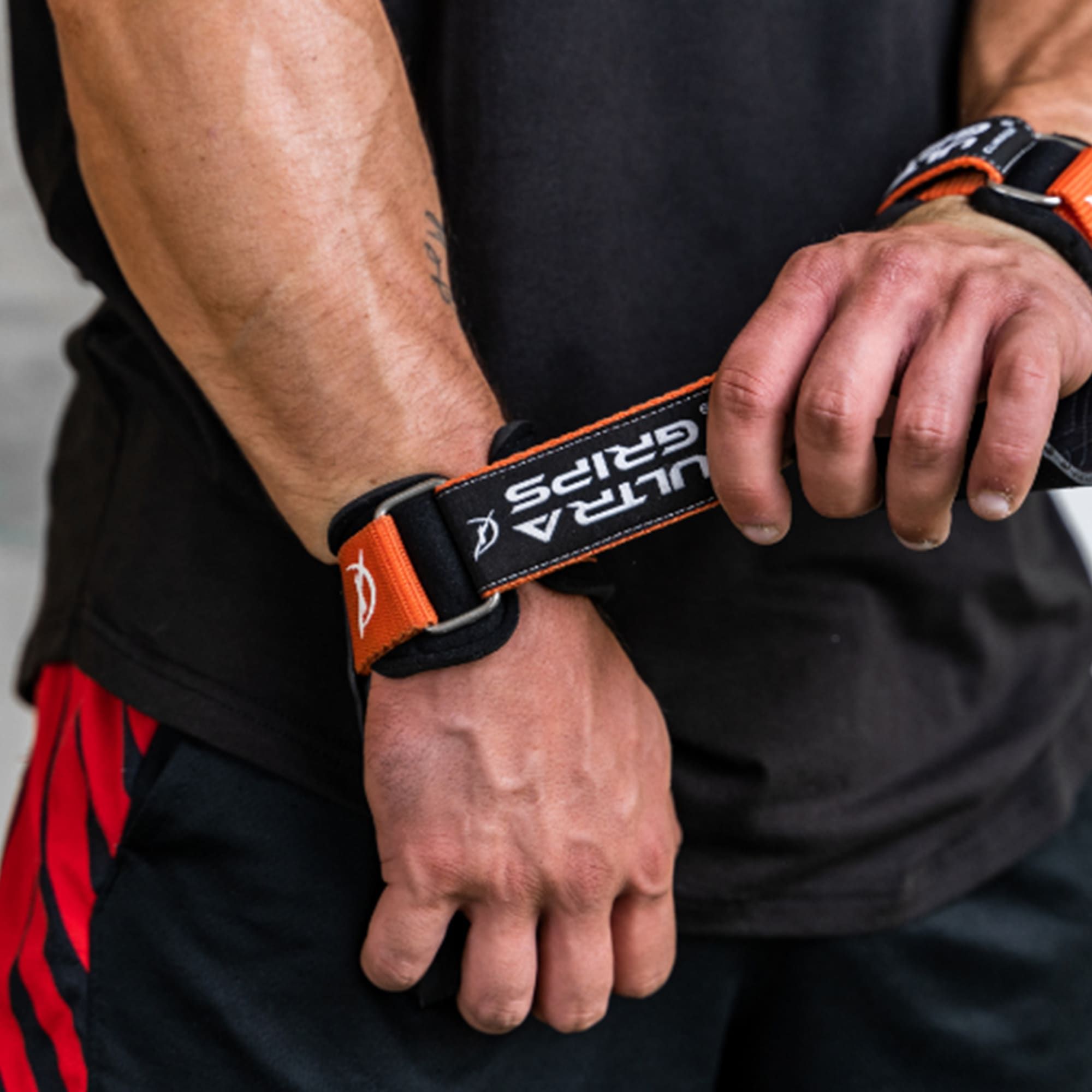 Person hält eine Ultra Grip. Schwarzes Band mit orangefarbenen Akzenten und "ULTRA GRIPS"-Schriftzug.