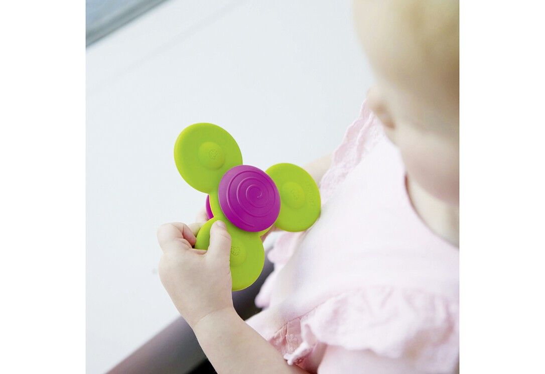 Ein Kind hält einen bunten Spinner in der Hand. Der Spinner besteht aus grünen und pinkfarbenen Scheiben.