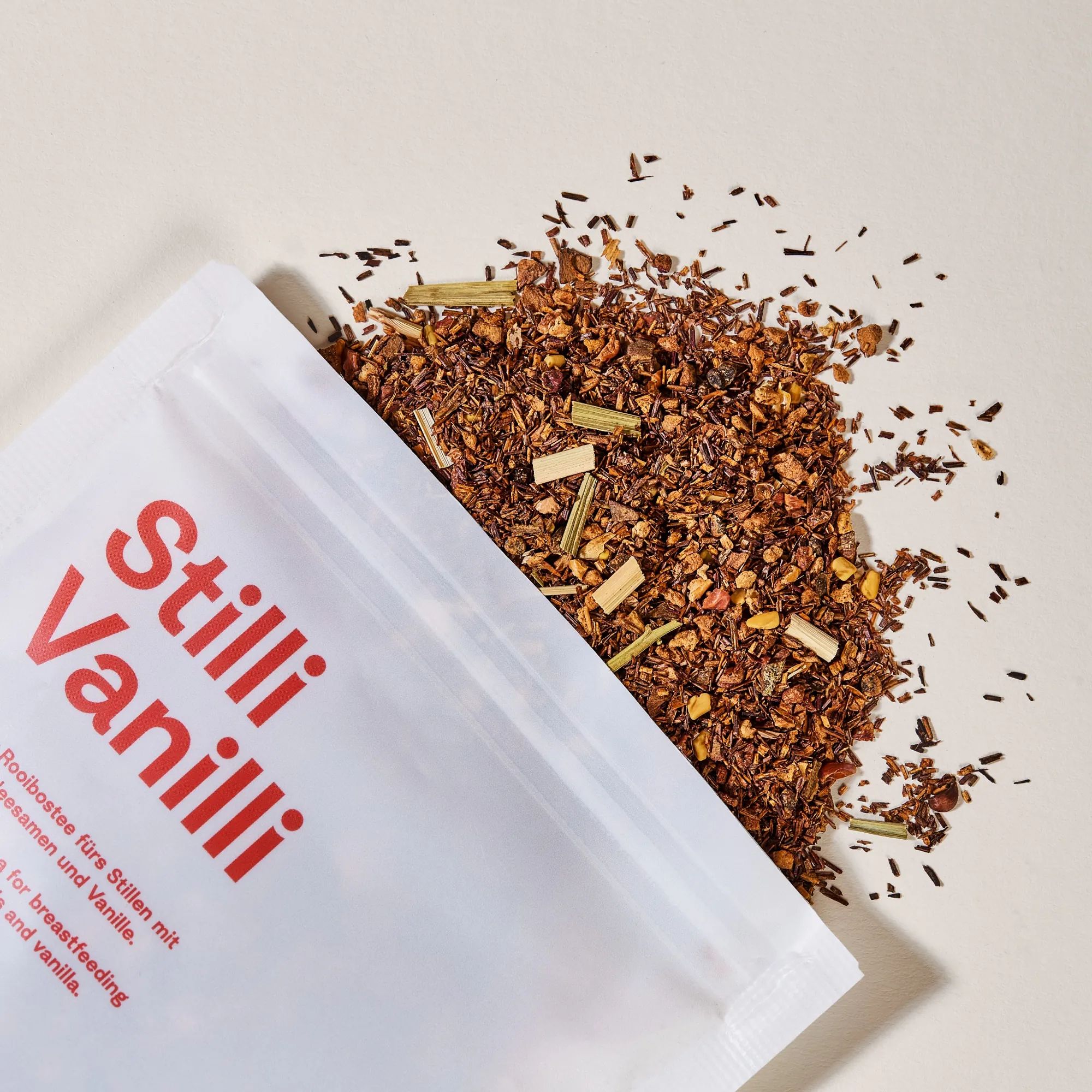 Geöffnete Packung Still-Tee Stilli Vanilli. Roter Text. Rooibos-Tee mit Kräutern. Tee daneben.