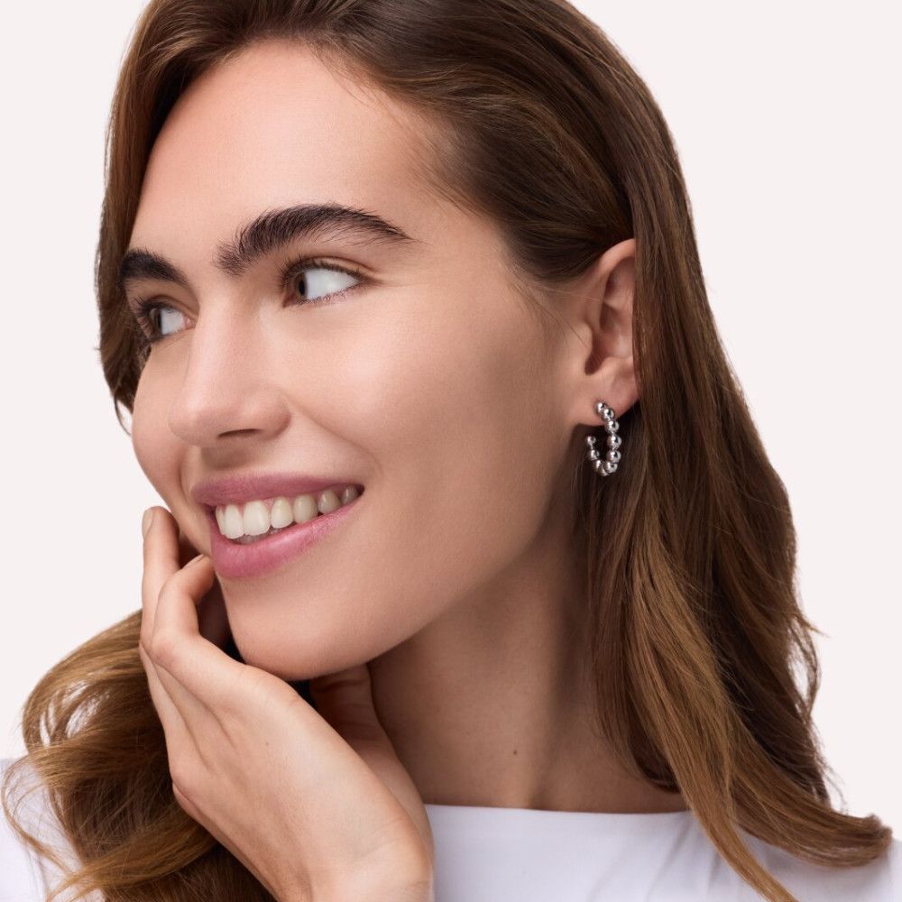 Porträt einer Frau mit langen, braunen Haaren. Sie trägt Ohrringe und lächelt. Der Hintergrund ist hell.