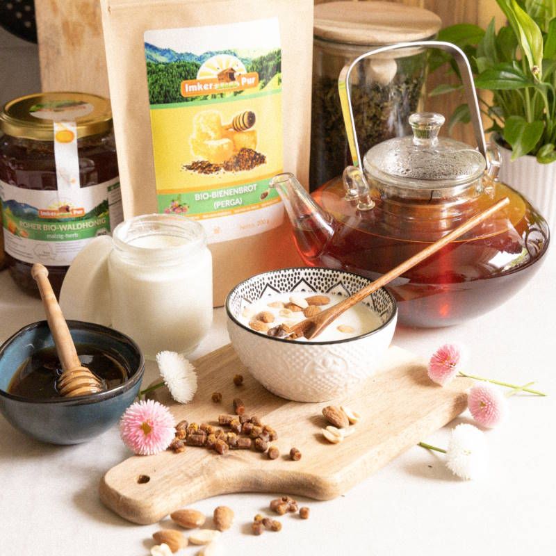 Stillleben mit Honig, Milch, Tee und ImkerPur Bio-Bienenbrot (Perga). Auf einem Holzbrett sind Mandeln und Blüten dekoriert.