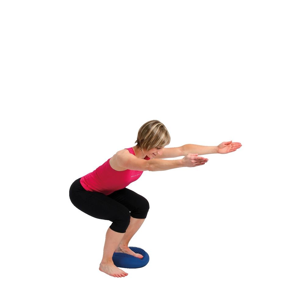 Frau macht Kniebeugen auf einem blauen Ballkissen. Sie hat die Arme ausgestreckt. Kissen ist rund.
