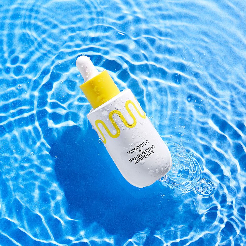 Weiße Pipettenflasche mit gelbem Verschluss, umgeben von Wasser. Enthält Vitamin C Brightening Ampoule.