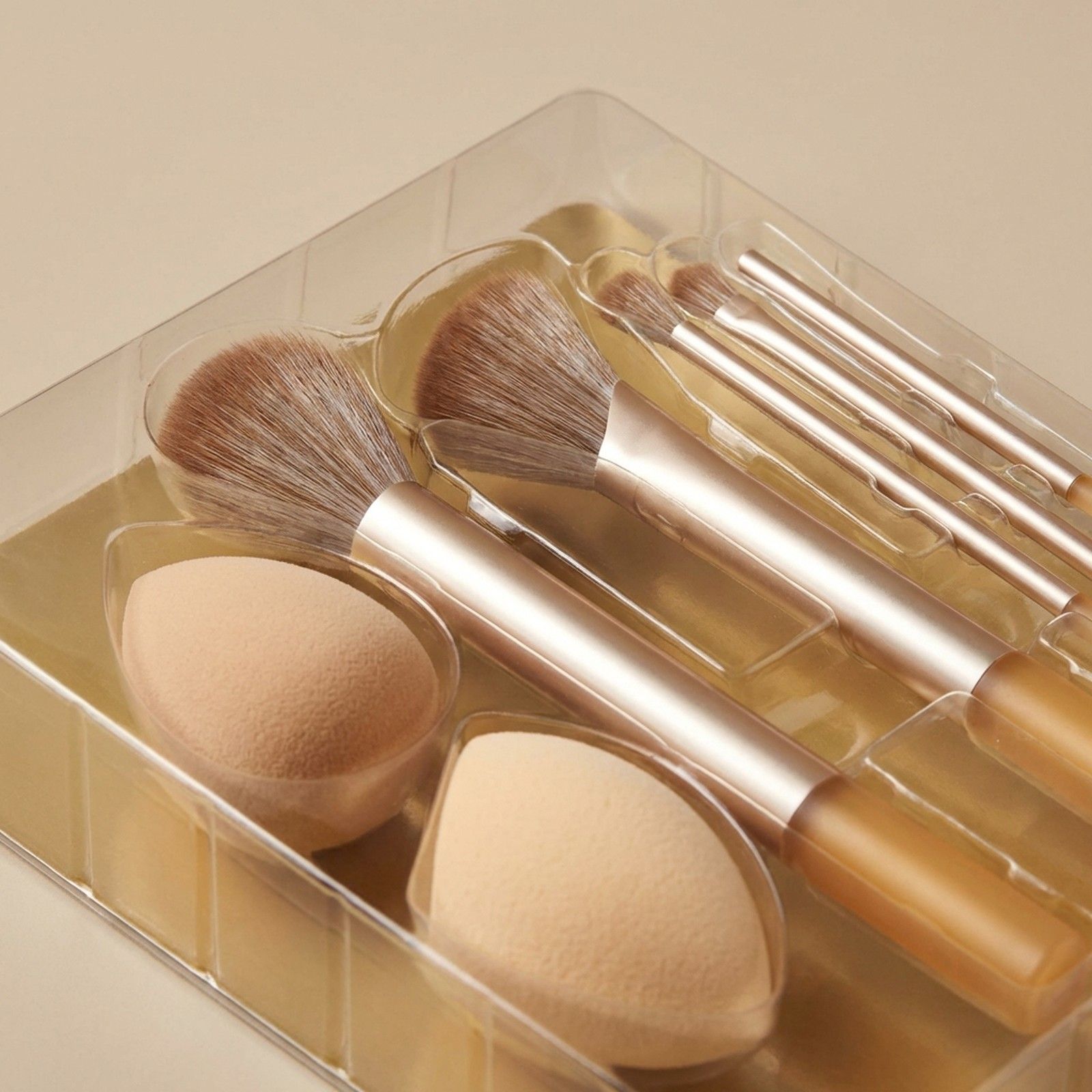 Set mit Make-up-Pinseln und Schwämmen in transparenter Verpackung. Goldene Griffe, braune Borsten.