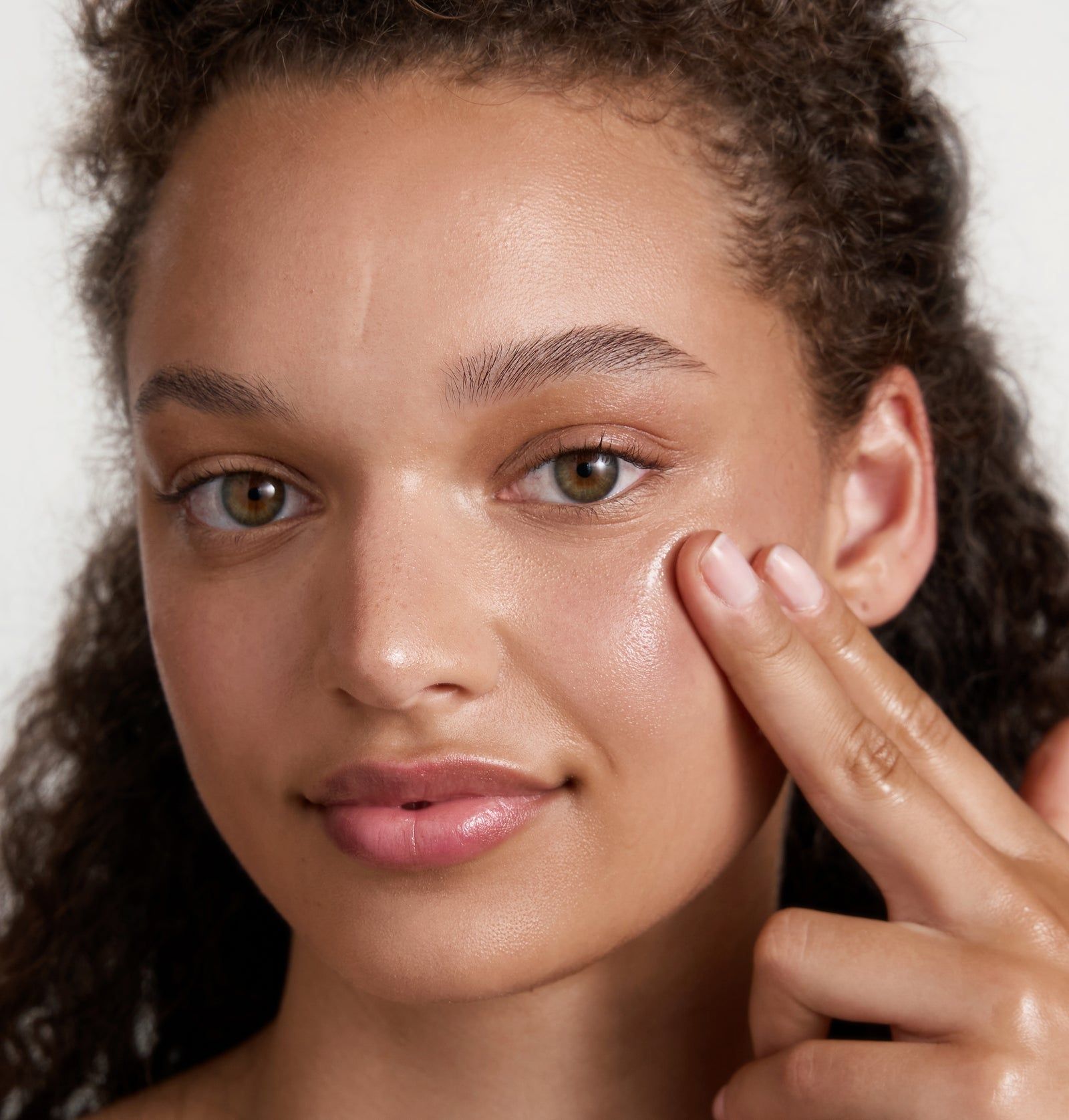 Frau berührt sanft ihre Wange. Haut wirkt glänzend. Helle Haut, dunkle Haare.