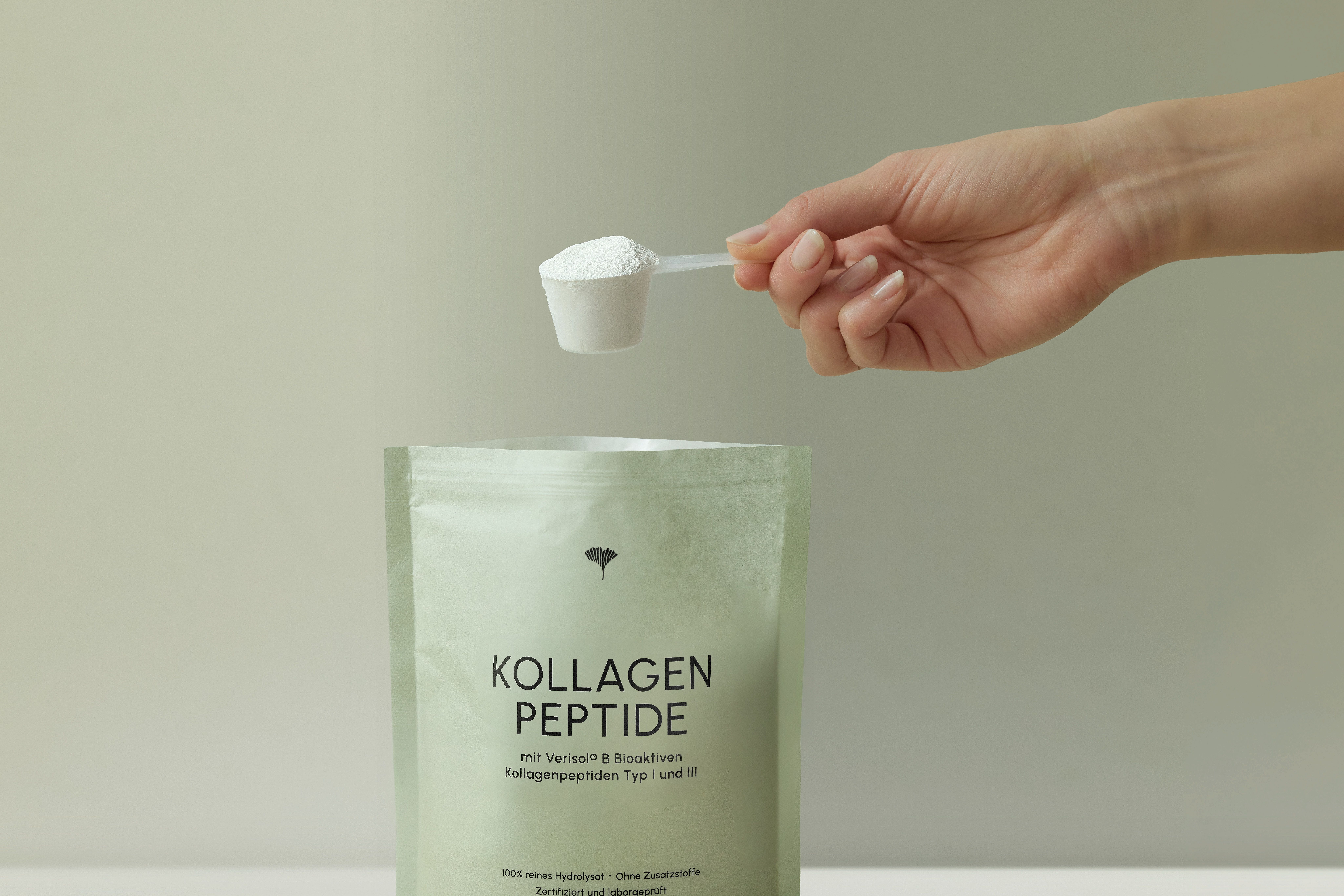 Hand hält Messlöffel mit VIANOA Kollagen Peptide Pulver über einem offenen Beutel.