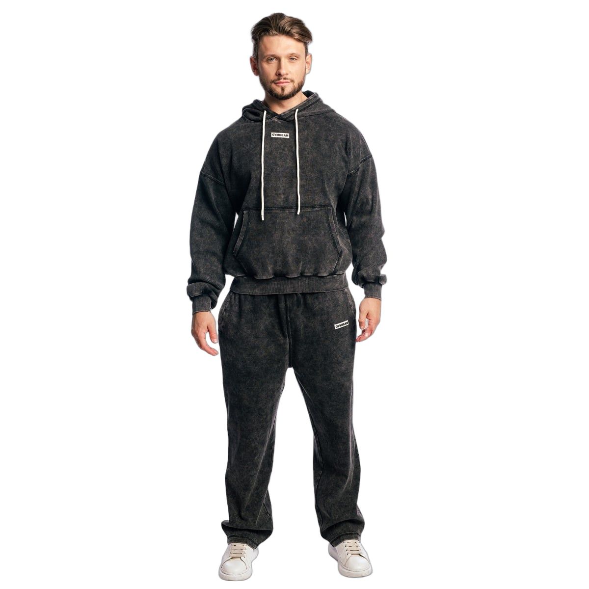 Mann trägt einen Oversized Hoodie und Jogginghose in verwaschenem Schwarz. Beide mit Logo-Patch.