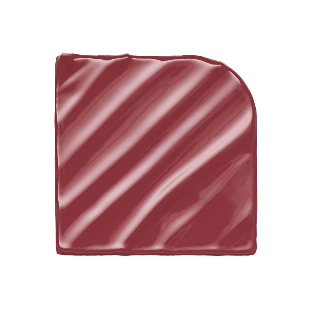 Quadratische, rote Lippenstiftprobe mit abgerundeter Ecke. Glänzende Oberfläche mit diagonalen Streifen.