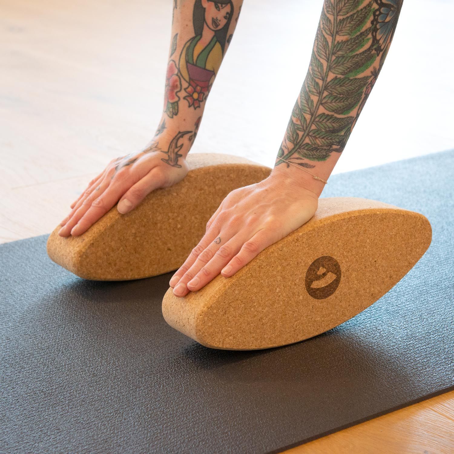 Zwei Kork-Ellipsen auf Yogamatte. Hände auf den Ellipsen. Tattoo-Arme.