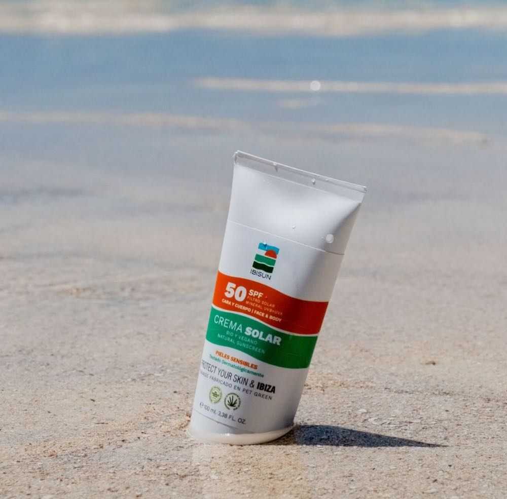 Sonnencreme-Tube im Sand. SPF 50+ und Produktbezeichnung 'Crema Solar' sichtbar.