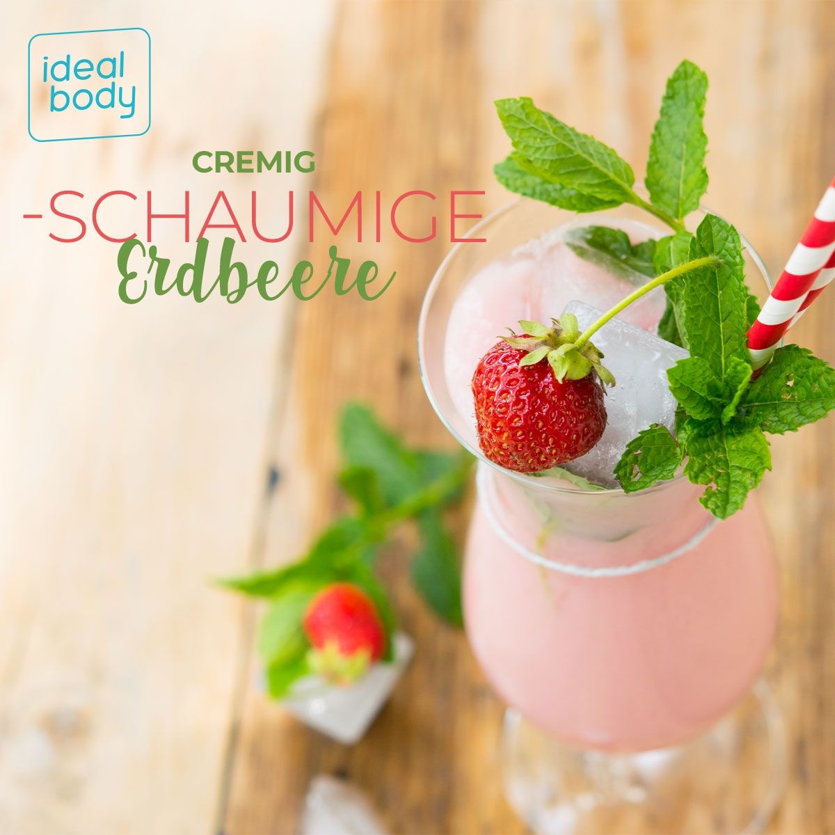 Glas mit Erdbeer-Shake, Eiswürfeln, Minze und Erdbeere. Roter Trinkhalm. Auf Holzuntergrund.