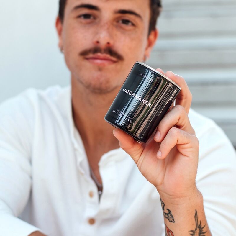 Person hält eine schwarze Kerze. Aufschrift: MATCHMAKER, PHEROMONE MASSAGE CANDLE.