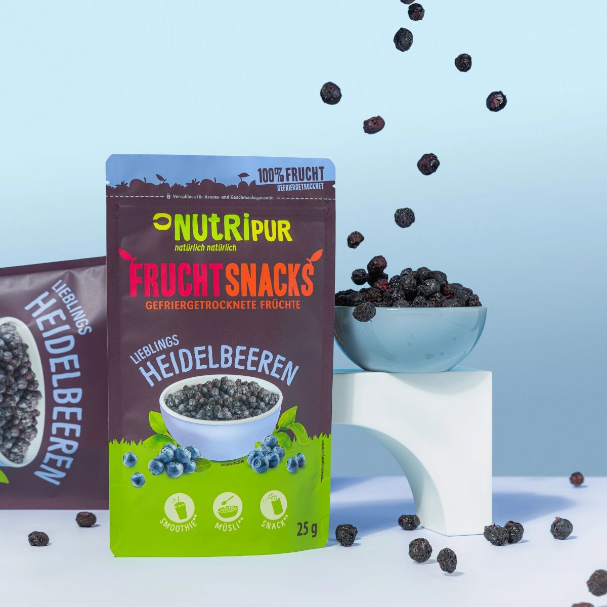 Beutel mit gefriergetrockneten Heidelbeeren, daneben Schale mit Beeren. Einige Beeren fallen. Marke NutriPur.
