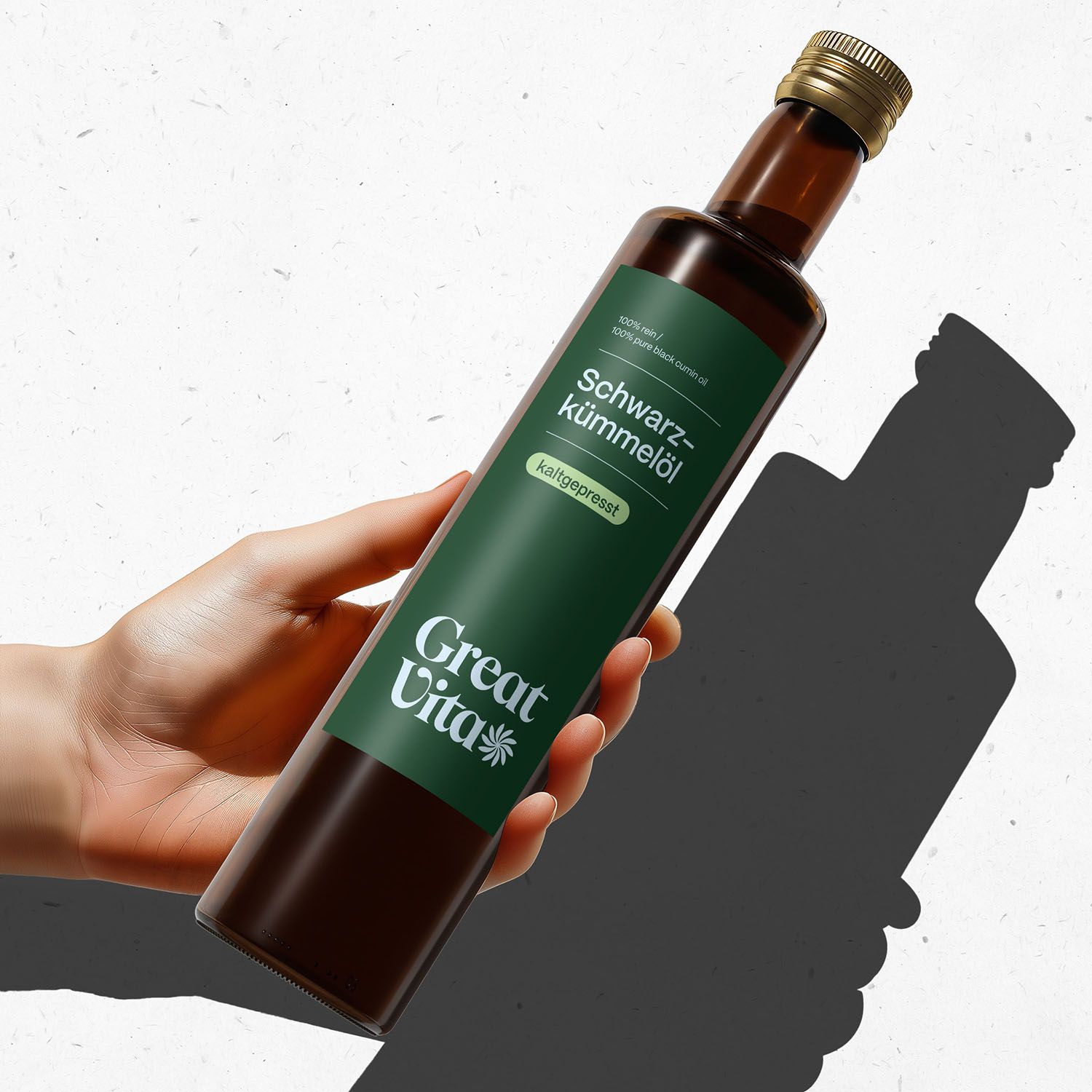 Eine Hand hält eine Flasche GreatVita Schwarzkümmelöl. Braune Flasche mit grünem Etikett und goldenem Verschluss. Schatten.