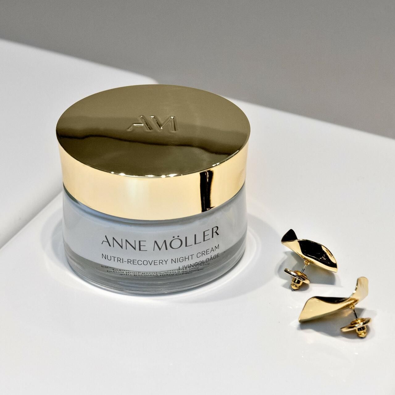 Creme-Tiegel mit goldenem Deckel und Ohrringen. Aufschrift: Anne Möller, Nutri-Recovery Night Cream, Livingoldâge.