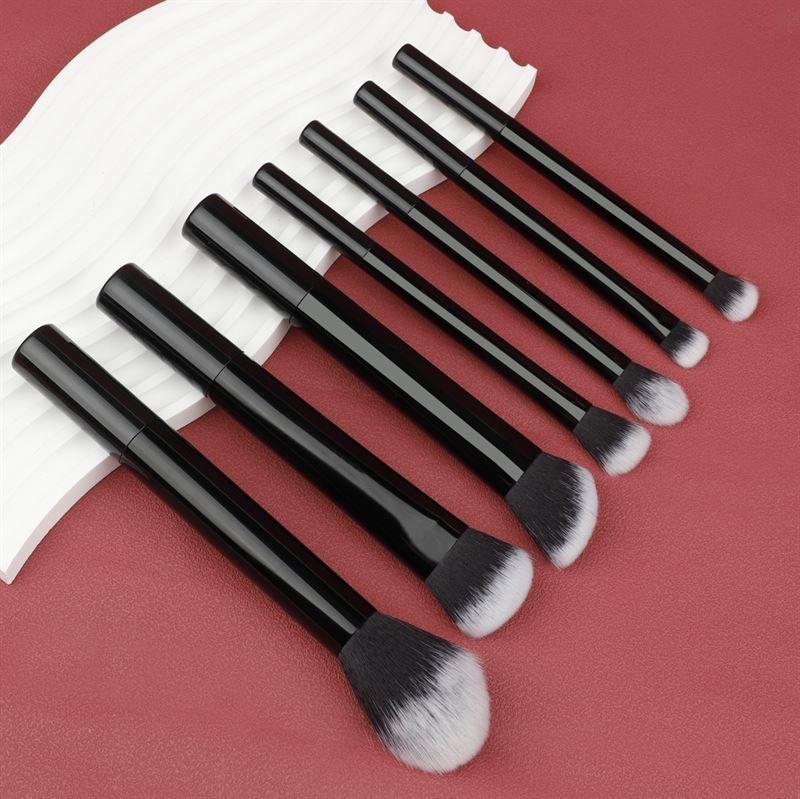 Sieben schwarze Make-up-Pinsel mit weißen Borsten, angeordnet auf rotem Hintergrund. Verschiedene Formen.
