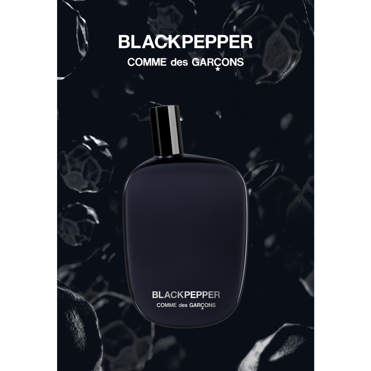 Schwarze Flasche mit schwarzem Verschluss. Aufschrift: Blackpepper, Comme des Garçons. Hintergrund mit schwarzen Formen.