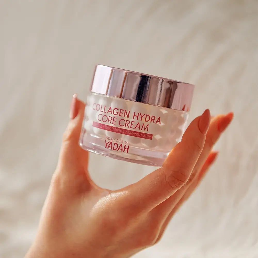Glasbehälter mit rosa Deckel. Aufschrift: Collagen Hydra Core Creme. Marke: YADAH. Hand hält Creme.