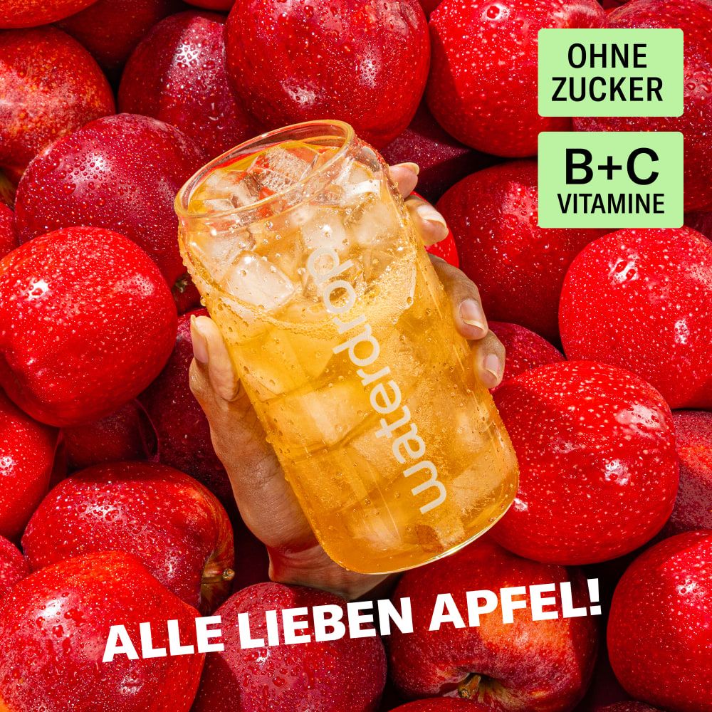 Hand hält ein Glas waterdrop® Microdrink Apfel, umgeben von Äpfeln. Ohne Zucker, B+C Vitamine.