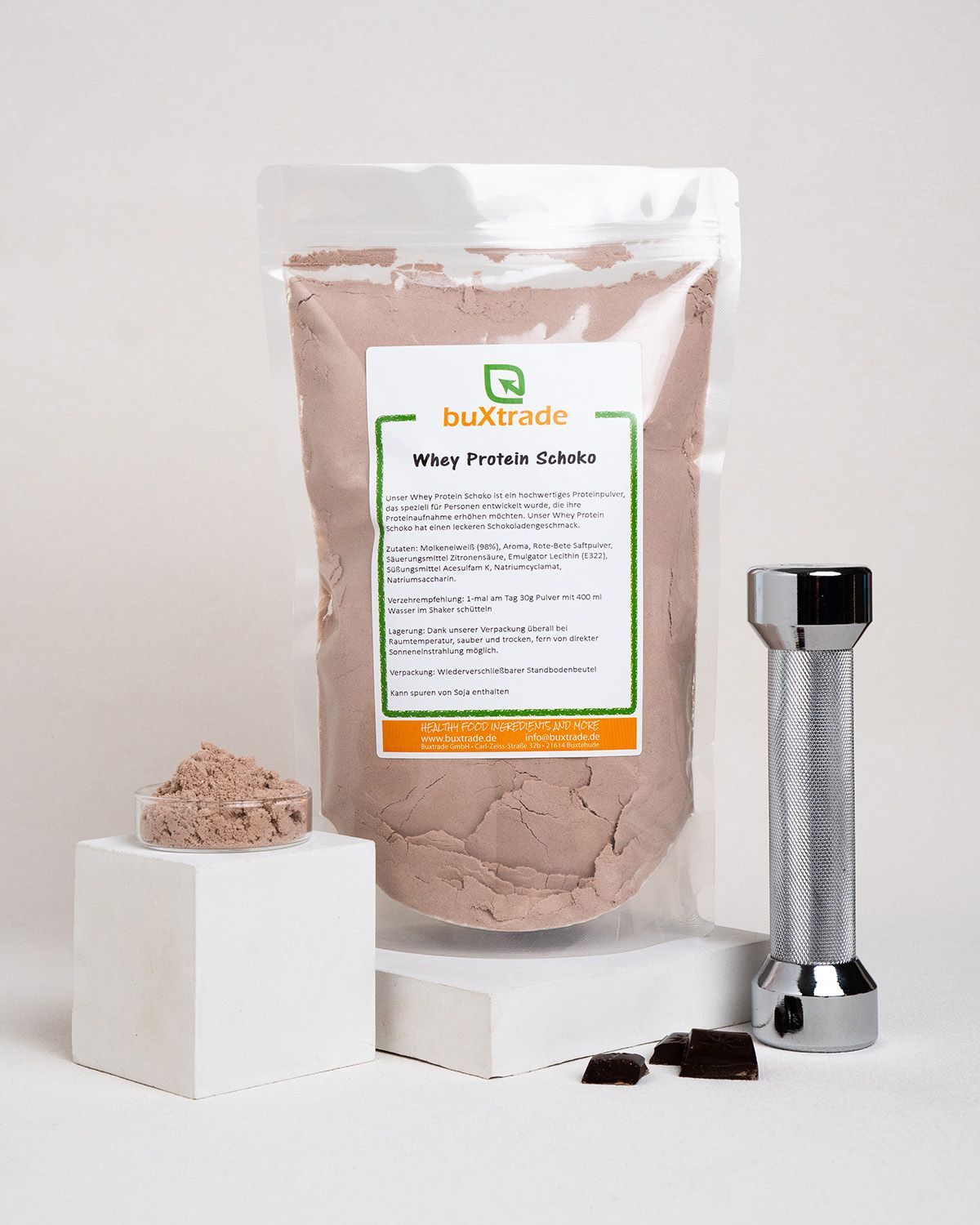 Beutel mit buXtrade Whey Protein Schoko, Schale mit Pulver, Schokoladenstücke und Metallstab.