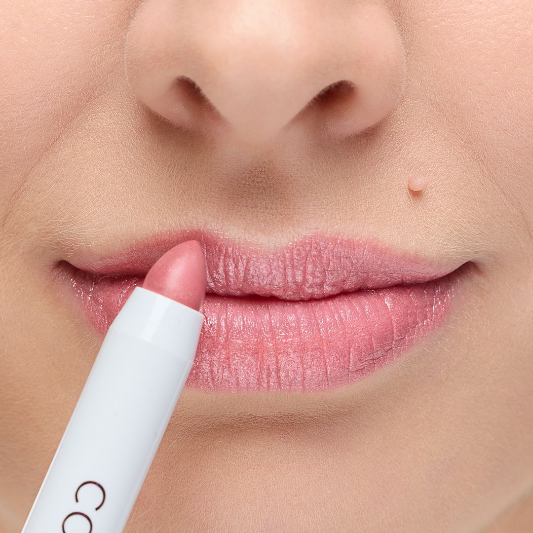 Lippenstift in Stiftform, hellrosa. Anwendung auf Lippen. Weißer Stift mit schwarzer Schrift.