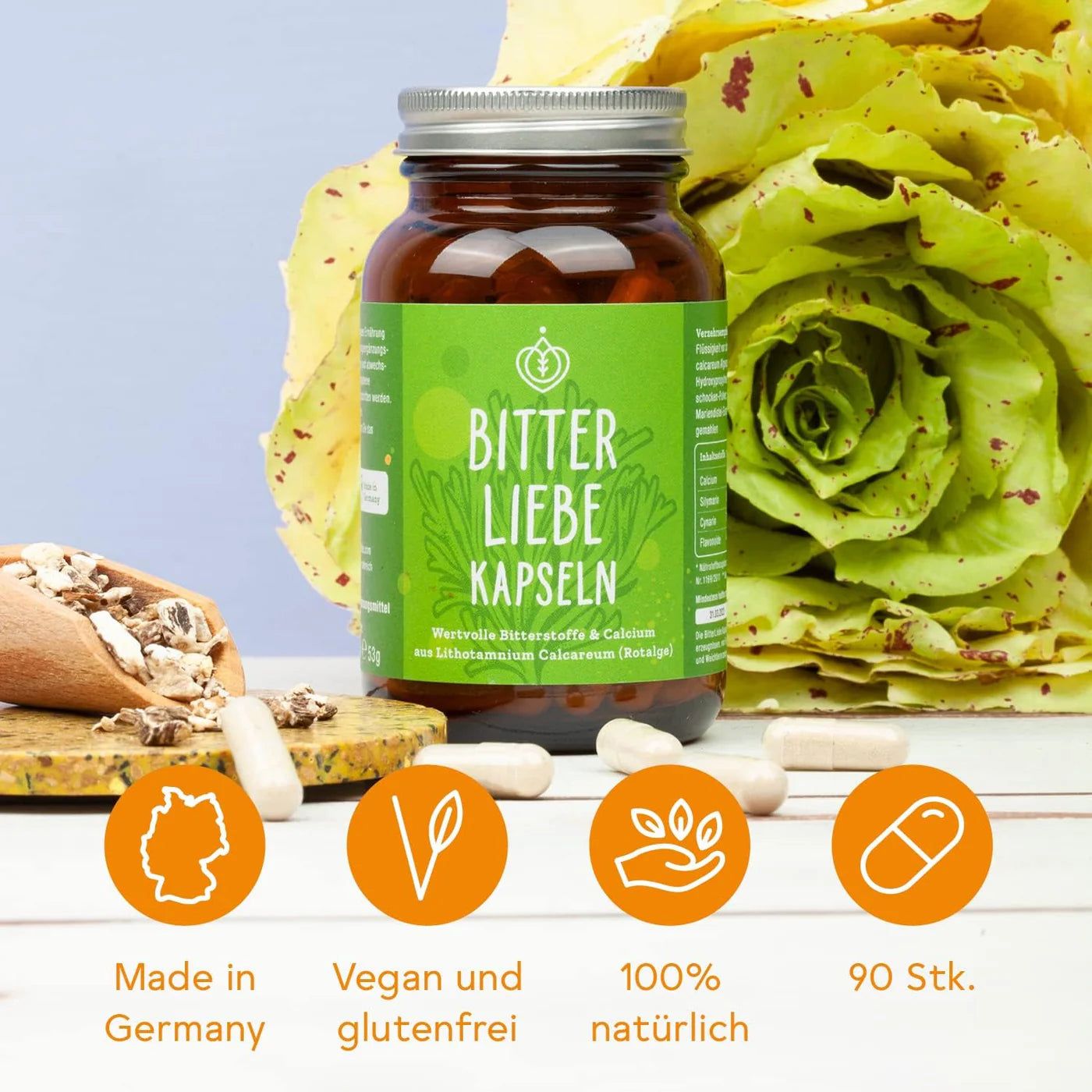Braune Glasflasche BitterLiebe Kapseln, daneben Kapseln, Holzlöffel mit Kräutern, grüne Blätter. Logos: Made in Germany, vegan, natürlich, 90 Stk.
