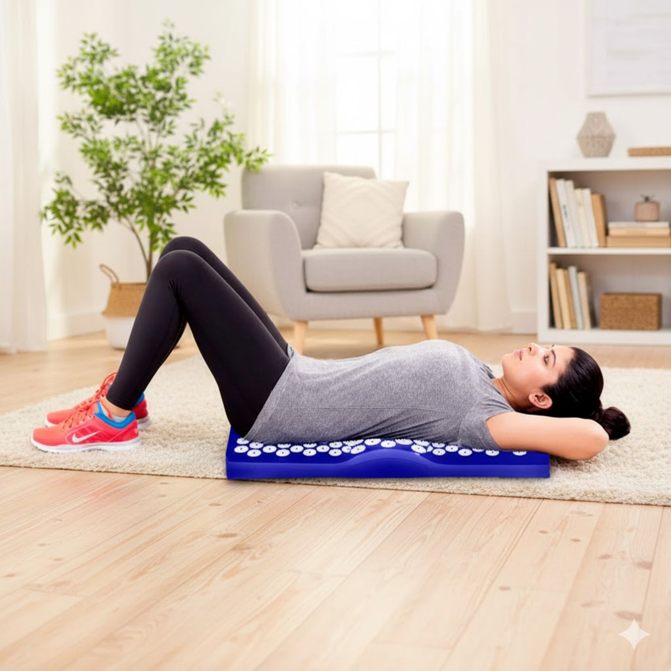 Person liegt auf blauer Akupressurmatte. Umgebung: Teppich, Couch, Pflanze. VITALIC Logo.