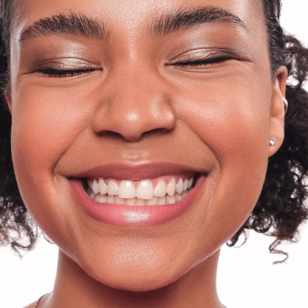 Nahaufnahme eines lächelnden Gesichts. Goldfarbener Lidschatten, rosa Lippen. Geschlossene Augen, weiße Zähne.