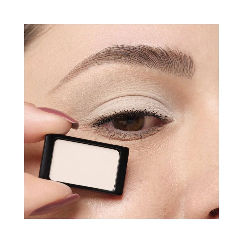 Helle, matte Lidschatten-Palette. Schwarzer Rahmen, beige Farbe. Gehalten vor einem Auge.