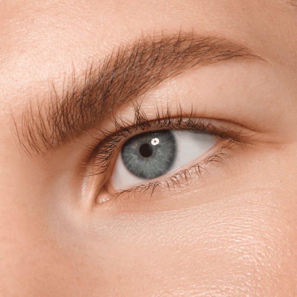 Nahaufnahme eines Auges mit buschigen Augenbrauen. Blaue Iris, helle Haut. Natürliches Aussehen.