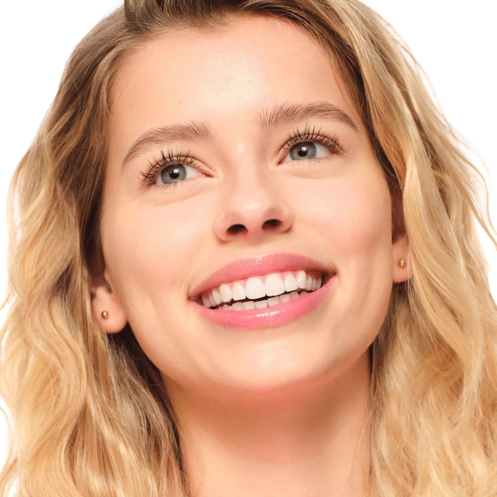 Porträt einer lächelnden Frau mit blonden Haaren. Sie hat blaue Augen und trägt Mascara.