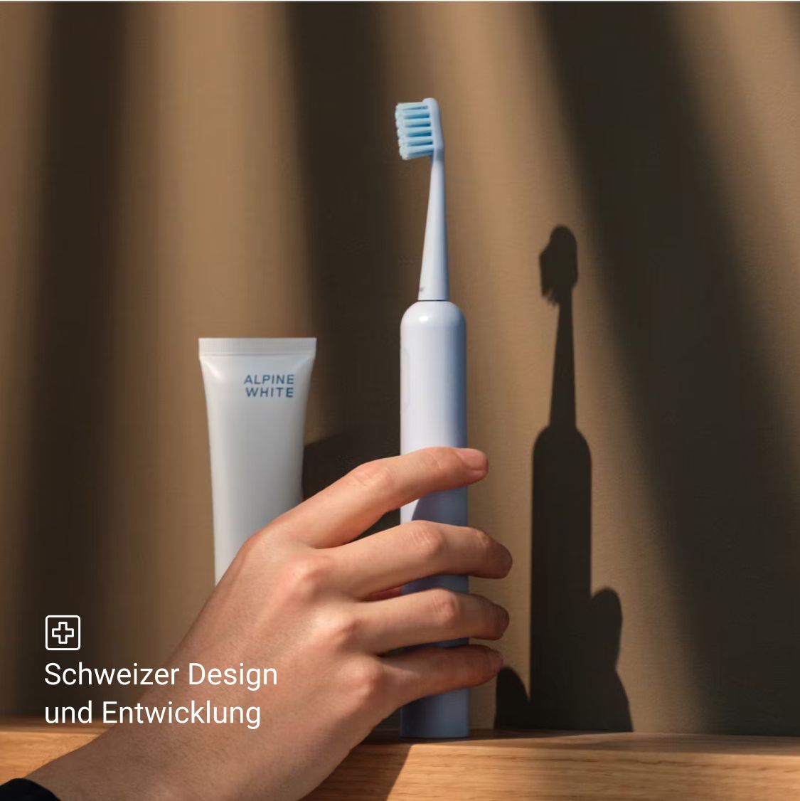 Eine blaue elektrische Zahnbürste, Zahnpasta und eine Hand. Schweizer Design und Entwicklung.