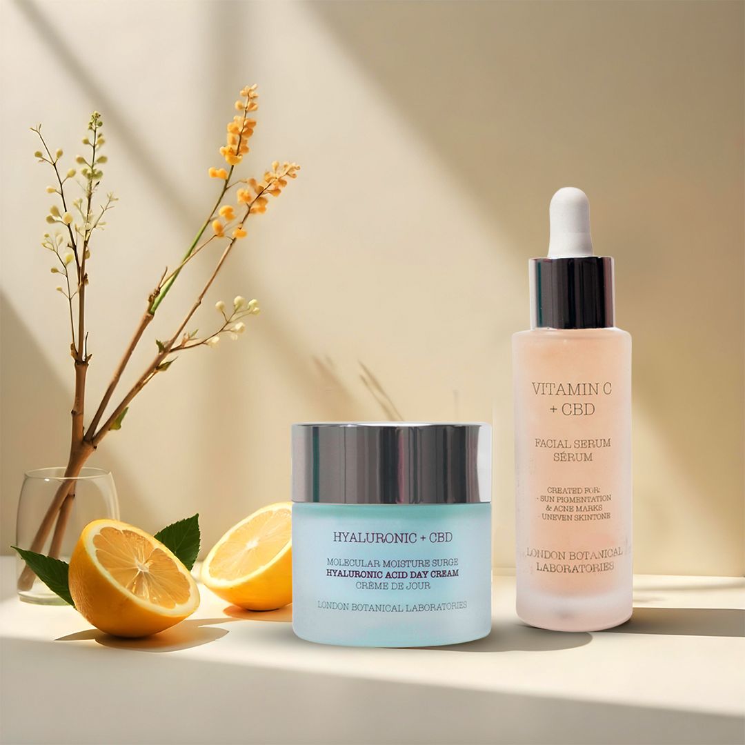 Creme- und Serumflasche neben Zitrone und Zweig. Aufschrift: Hyaluronic + CBD, Vitamin C + CBD.