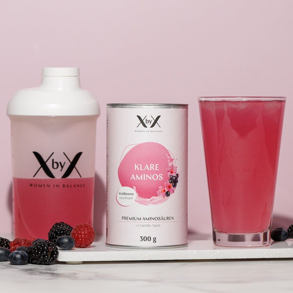 Dose und Shaker mit pinkfarbenem Getränk. Beeren liegen davor. Dose mit Aufschrift "XbyX Klare Aminos".